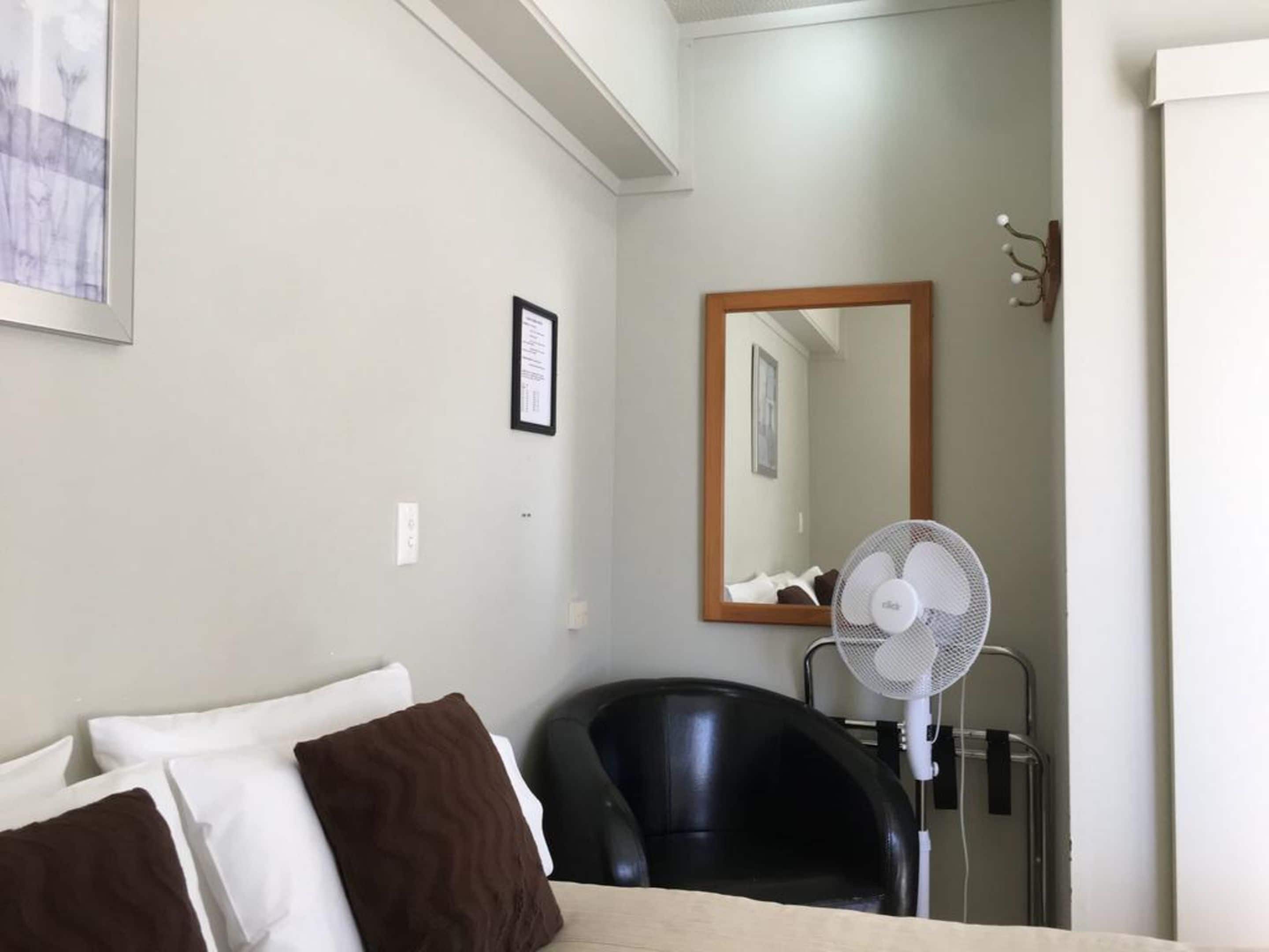 Een hotelkamer met een bed, een stoel, een ventilator en een spiegel aan de muur.