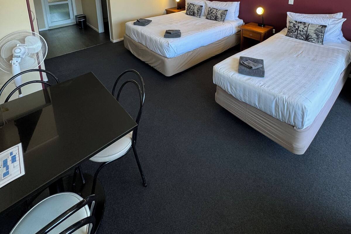 A hotel room with two beds, a dining table, chairs, and a TV.