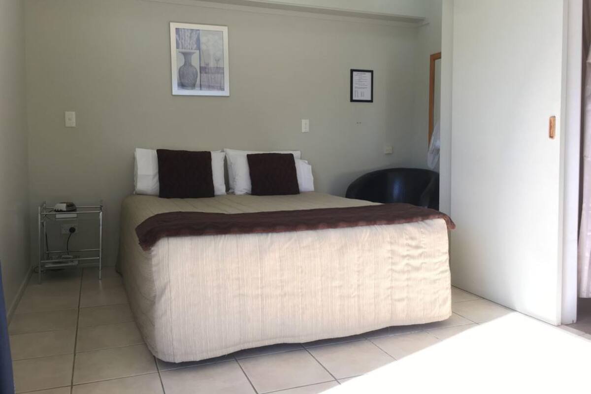A bedroom with a bed, a chair, a small table, and a picture on the wall.