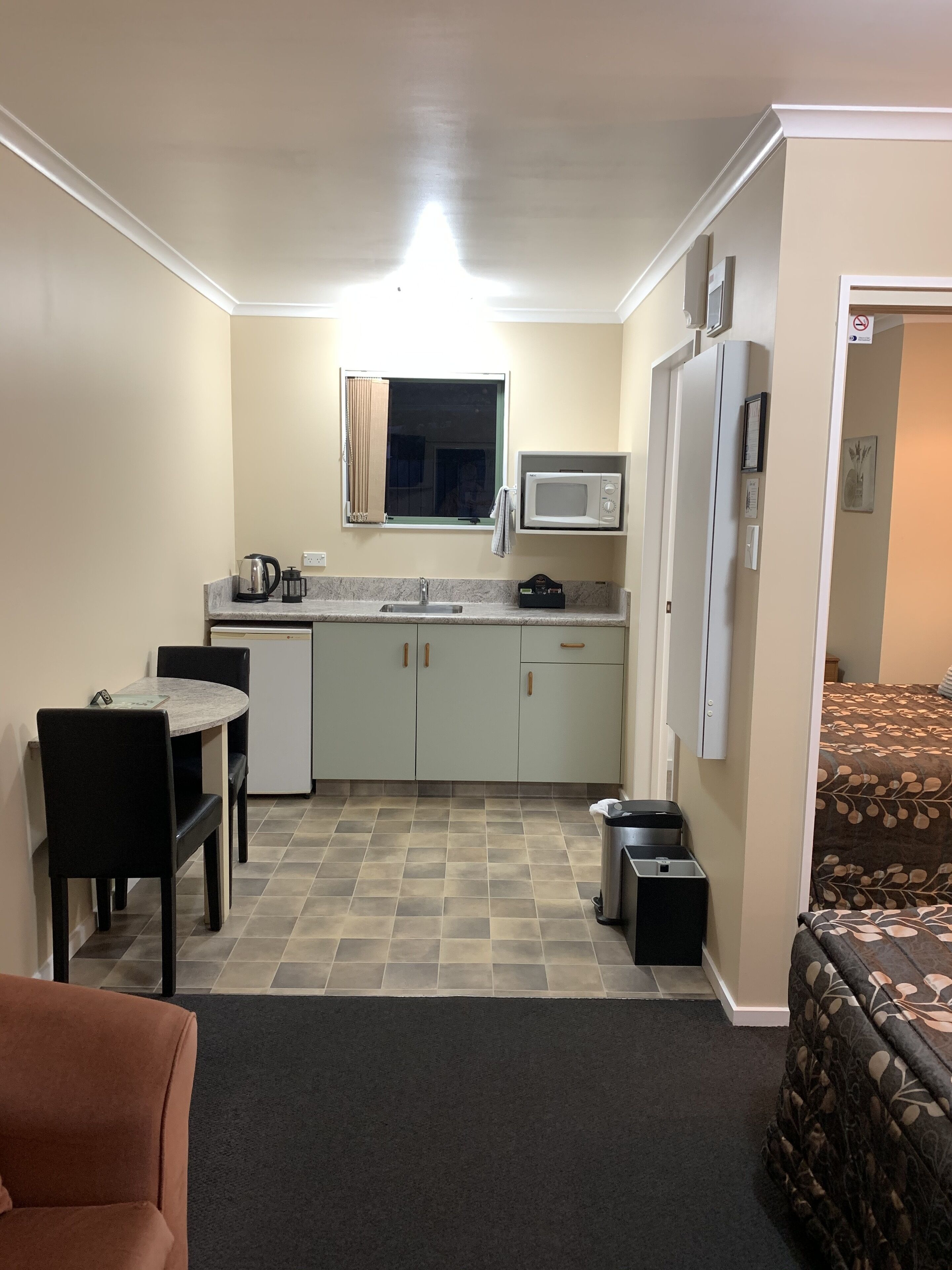 A compact kitchen with a microwave, kettle, and sink. There is a dining table with chairs and a small sofa in the living area.