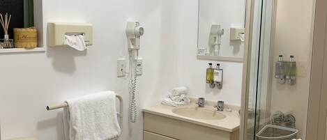 Un baño con inodoro, lavamanos y ducha. Cuenta con un perchero, un espejo y un box de ducha de vidrio.