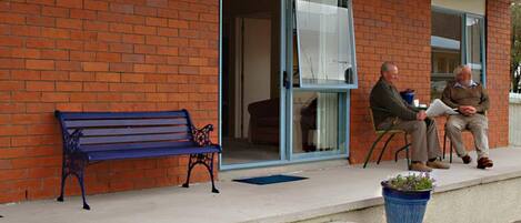 A brick building with a blue bench outside, a glass door, and two potted plants.