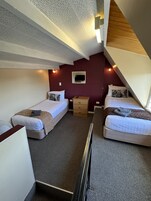 Habitación de hotel pequeña con dos camas individuales, un pequeño aparador de madera, un televisor montado en la pared y un techo con diseño perforado.