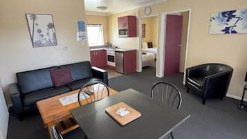 Een functionele ruimte met een eettafel, stoelen, een bank, een kitchenette en een afzonderlijke slaapruimte.