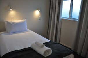 A neatly made bed with white linens, a rolled towel, and two wall-mounted lights.
