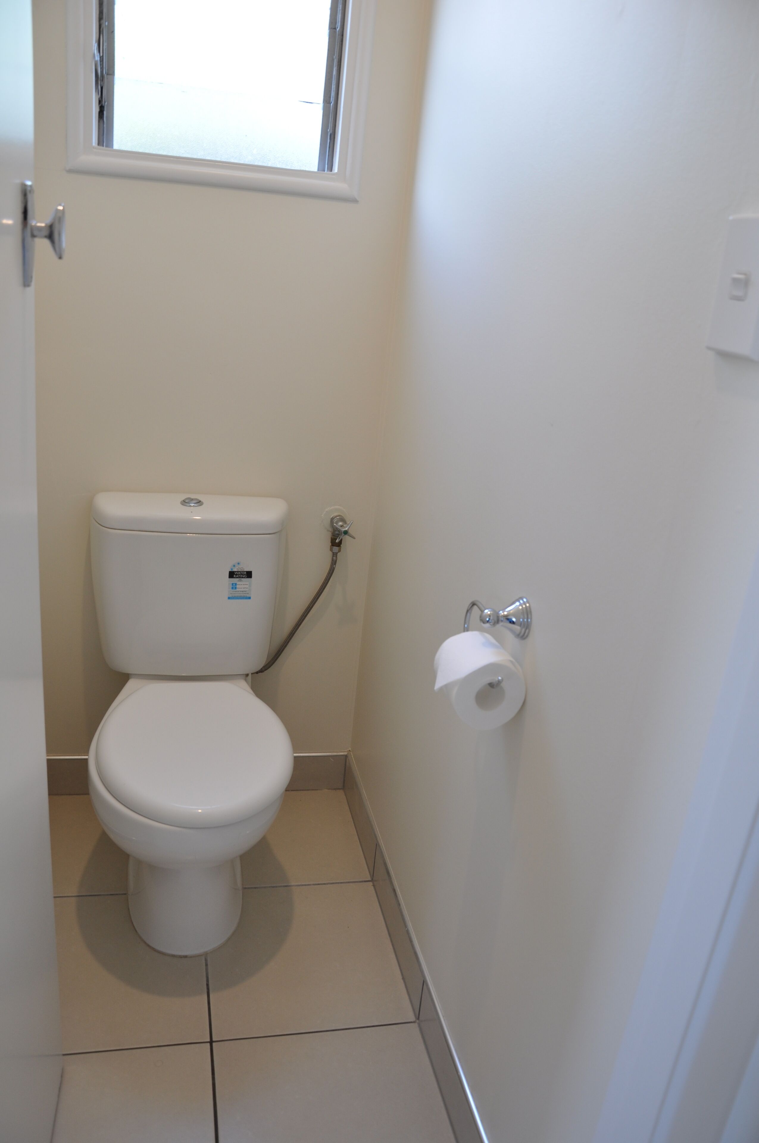 Un baño pequeño y limpio con inodoro, ventana y dispensador de papel higiénico.