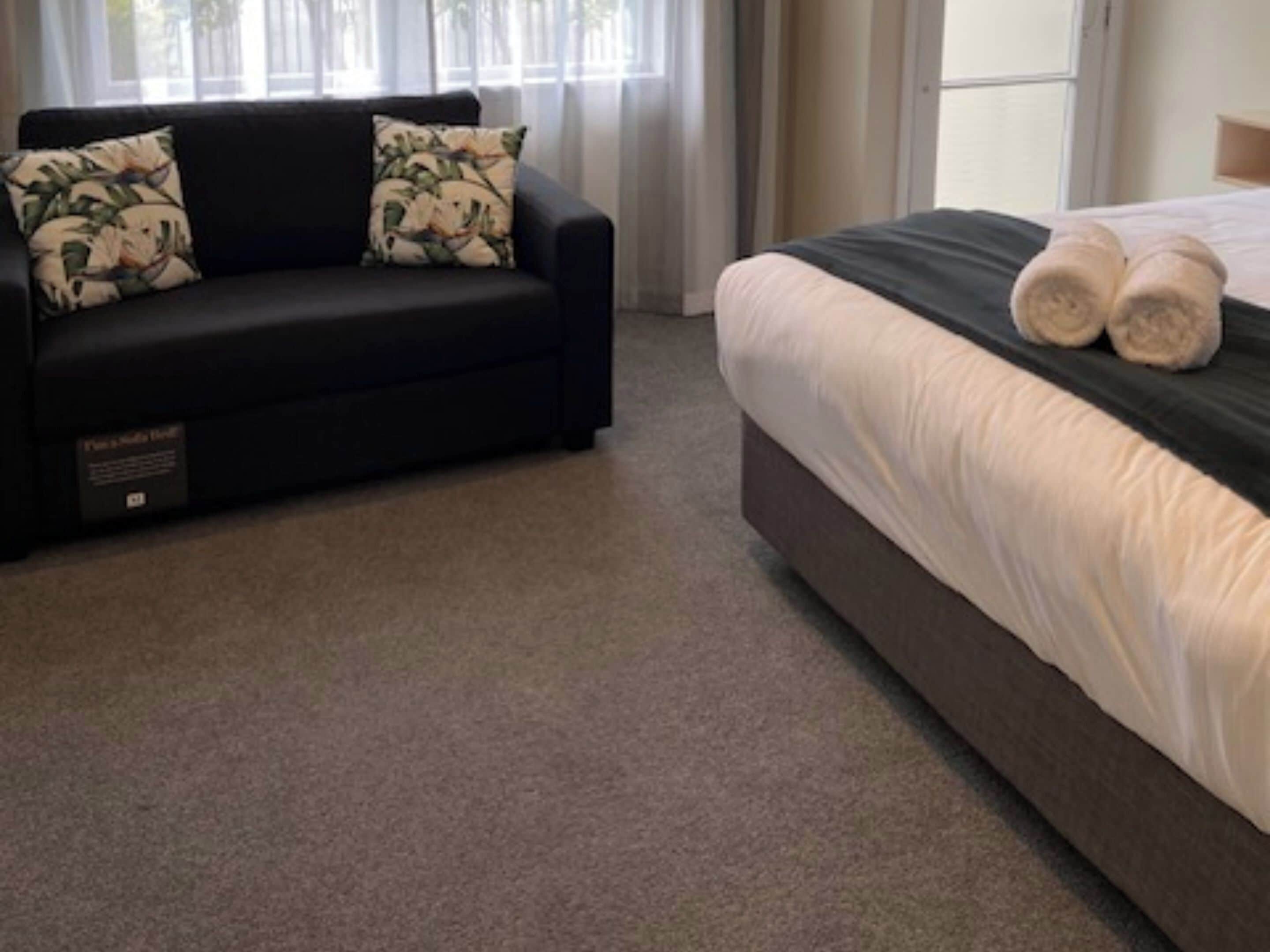 A hotel room with a dark sofa and a bed with white bedding.
