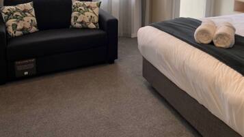 A hotel room with a dark sofa and a bed with white bedding.