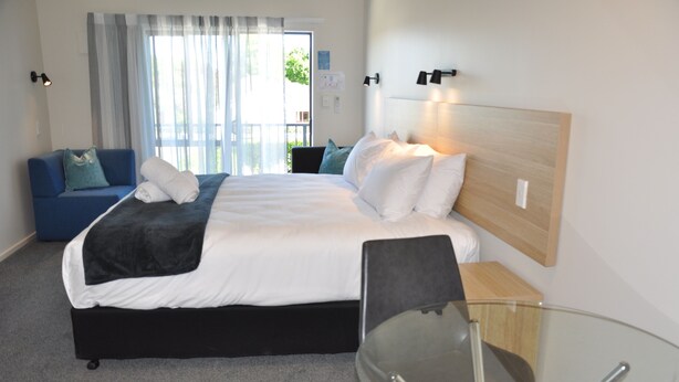 A hotel room with a bed, a glass table, a blue sofa, and a view of the outdoors. - Balmoral Motel (Nelson)