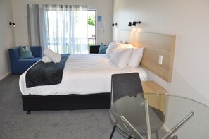 Quarto de hotel com uma cama, mesa de vidro, sofá azul e vista para o exterior.
