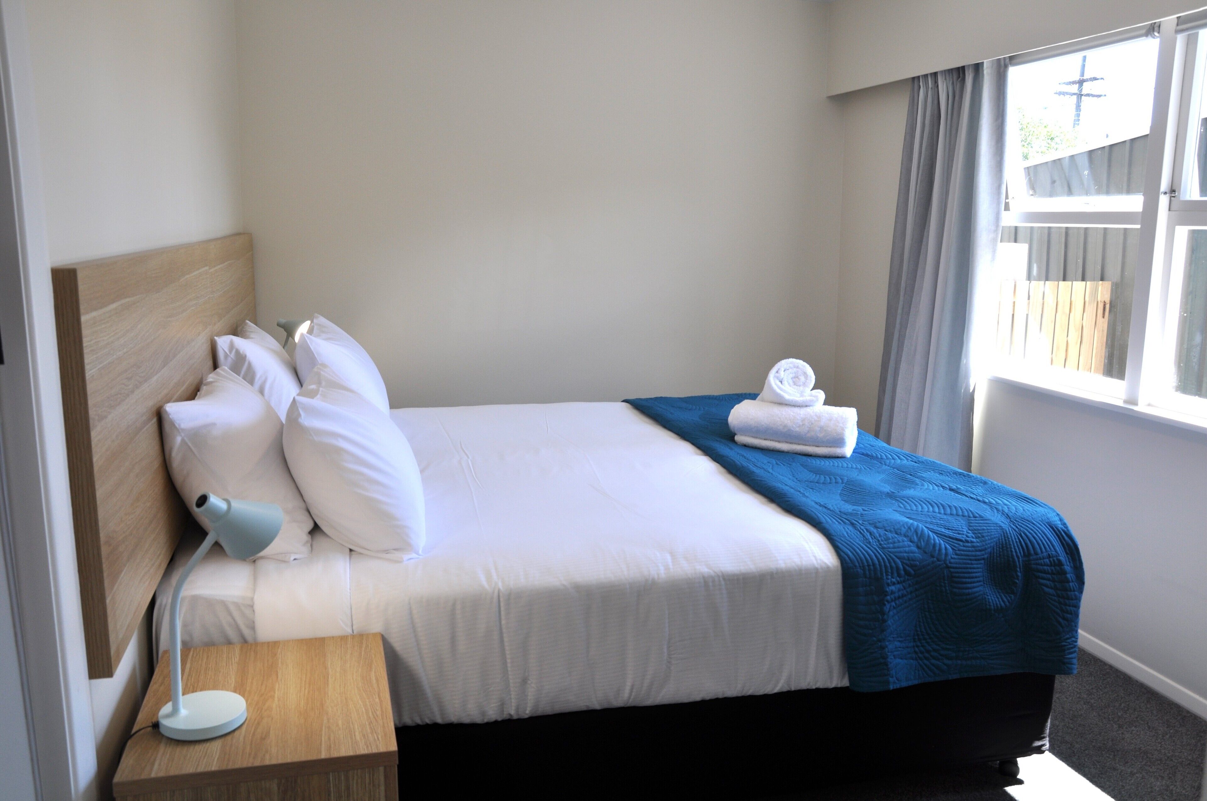 A neatly made bed with white linens, a blue blanket, and a wooden headboard.