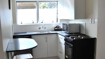 A compact kitchen with a sink, stove, microwave, and a small dining area with a stool.