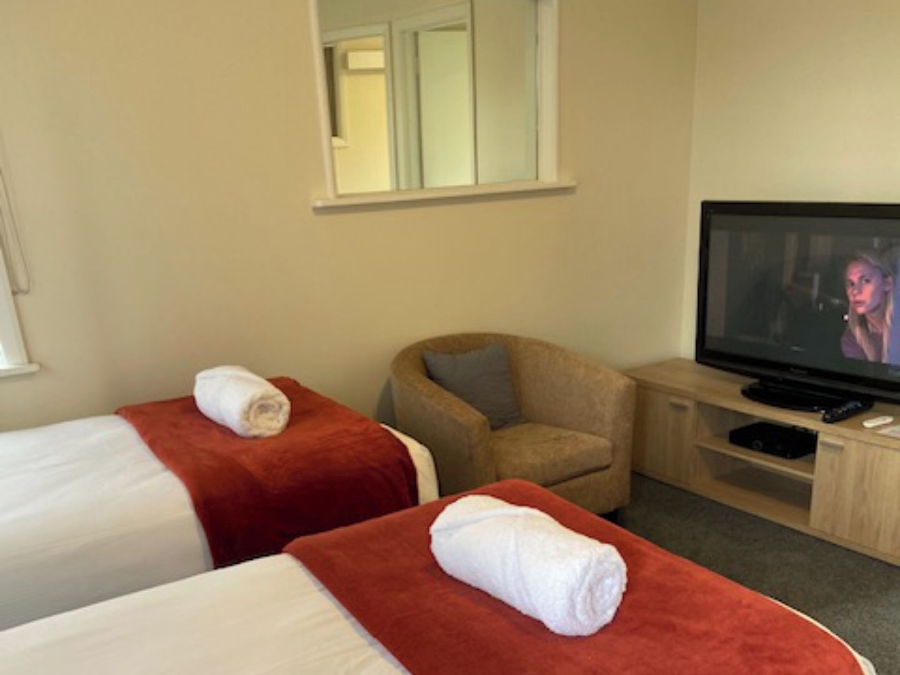 A hotel room with two beds, a TV, a chair, and a small table.