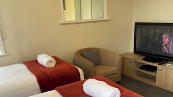 A hotel room with two beds, a TV, a chair, and a small table.