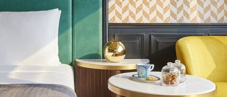 Una habitación de hotel con un cabecero verde, una mesa redonda con una lámpara dorada y un sillón amarillo.