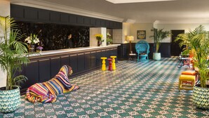 A lobby with a reception desk, patterned carpet, hanging chandeliers, and colorful seating. - The Connaught, New Delhi - IHCL SeleQtions (New Delhi)