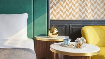 A hotel room with a green headboard, a round table with a gold lamp, and a yellow armchair.