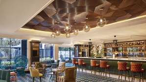 A bar area with multiple seating options, a bar counter with bottles, and a view through large windows. - The Connaught, New Delhi - IHCL SeleQtions (New Delhi)