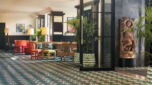 A spacious lobby with a patterned carpet, a seating area with a sofa and chairs, and a large window with a view. - The Connaught, New Delhi - IHCL SeleQtions (New Delhi)