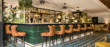 Zona de bar con taburetes verdes, suelo de baldosas y barra con estantes llenos de botellas.
