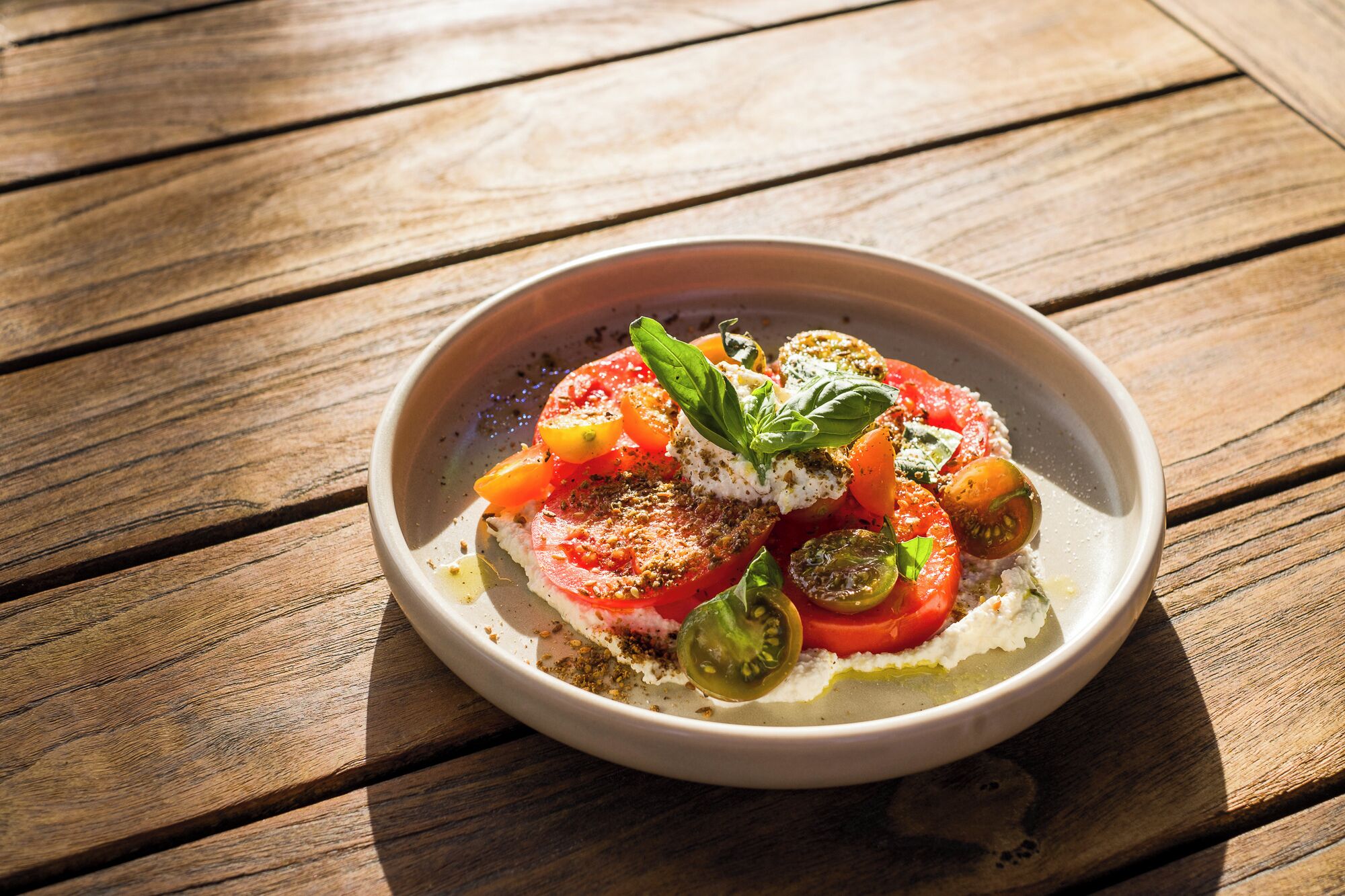 A bowl of Caprese salad on a wooden table.
