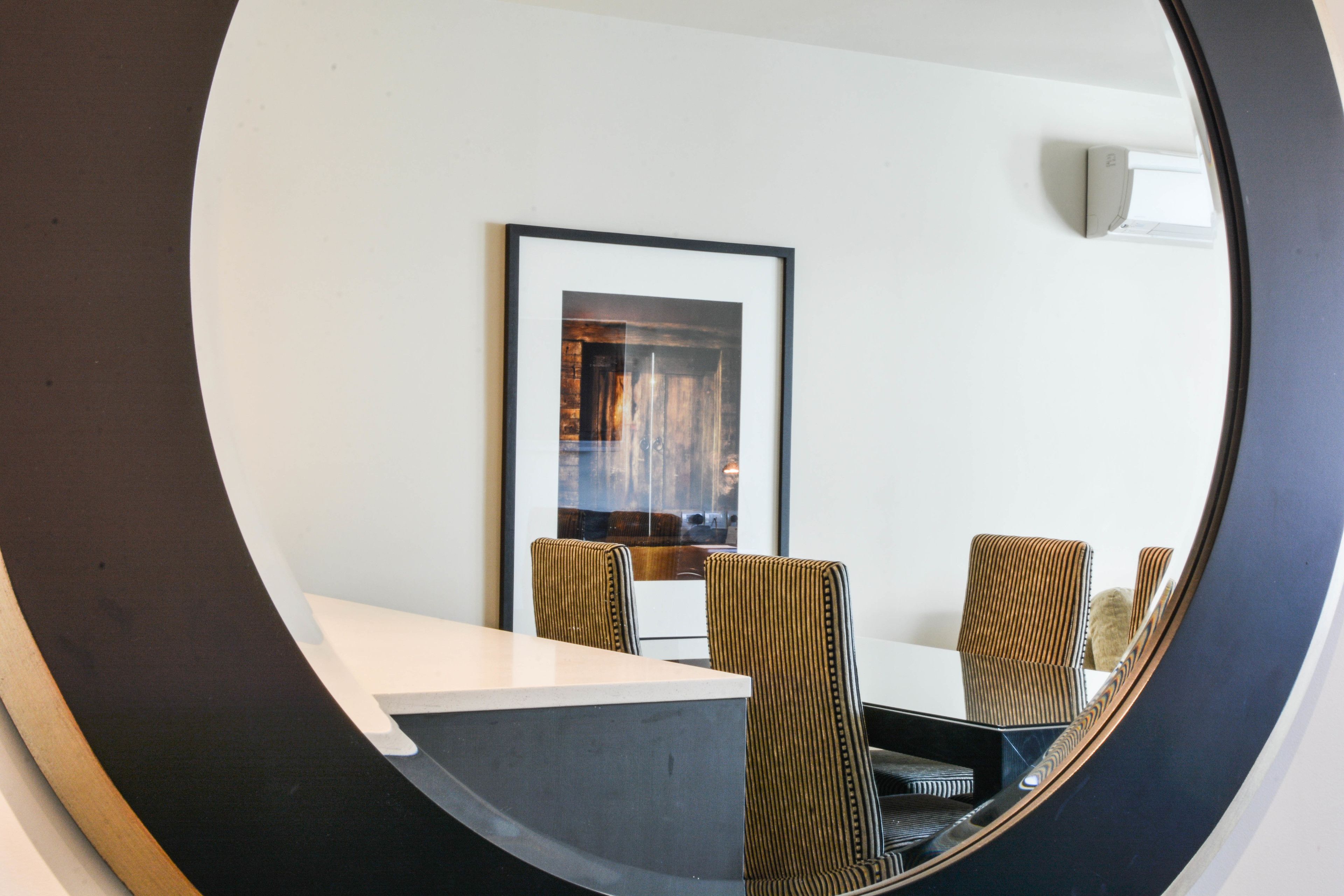 A dining area with a round table and chairs, a framed picture on the wall, and a ceiling-mounted light fixture.