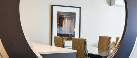 A dining area with a round table and chairs, a framed picture on the wall, and a ceiling-mounted light fixture.