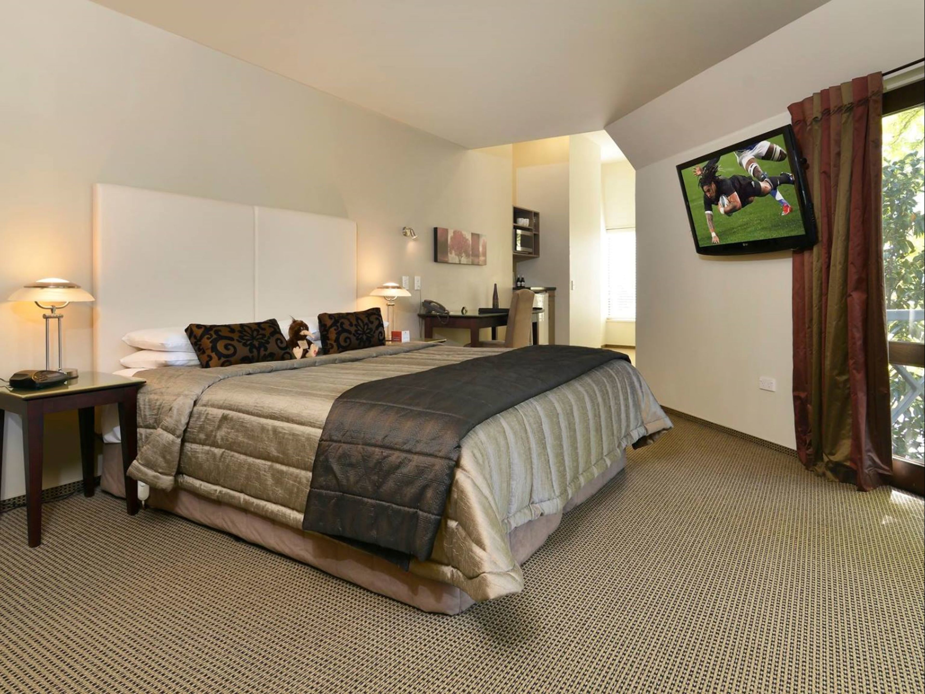 A hotel room with a large bed, a desk, a chair, a TV, and a window with curtains.