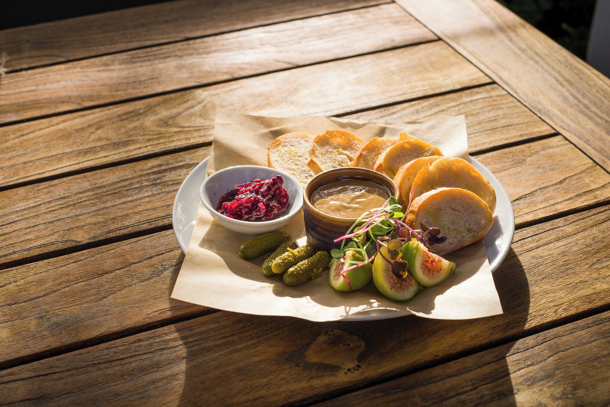 Una mesa de madera con un plato de comida que incluye pan, encurtidos y un bol de salsa.