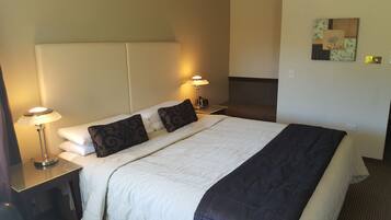 A hotel room with a large bed, two bedside tables, a nightstand, a wall-mounted lamp, and a decorative piece on the wall.