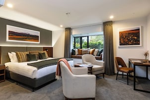 Una habitación de hotel con una cama, un sofá, una silla, una mesa y dos ventanas.