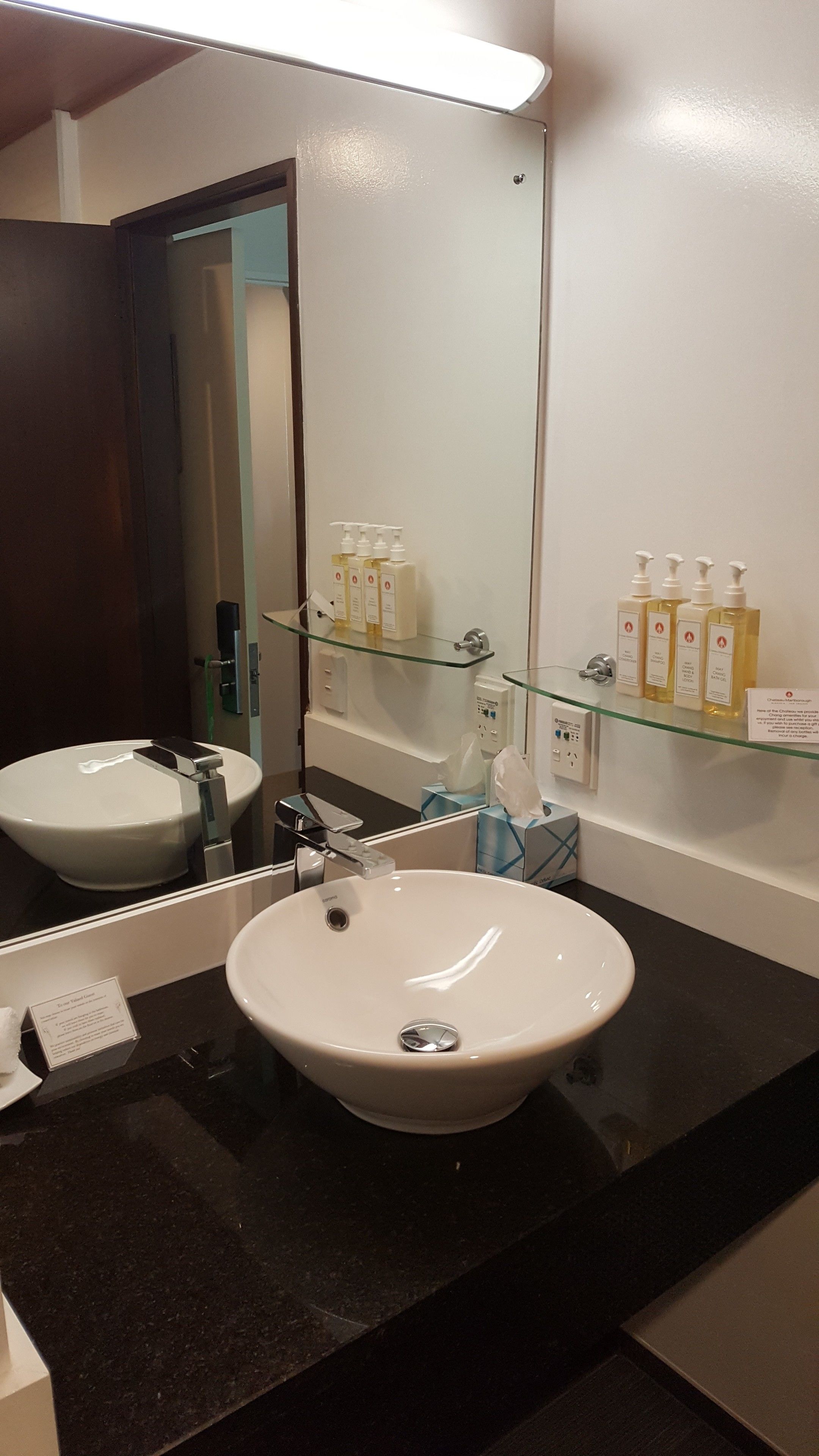 A bathroom with a white sink, a mirror, and a glass shelf with toiletries.