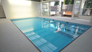 Una grande piscina interna con acqua cristallina e azzurra, circondata da un pavimento piastrellato e pareti in vetro.