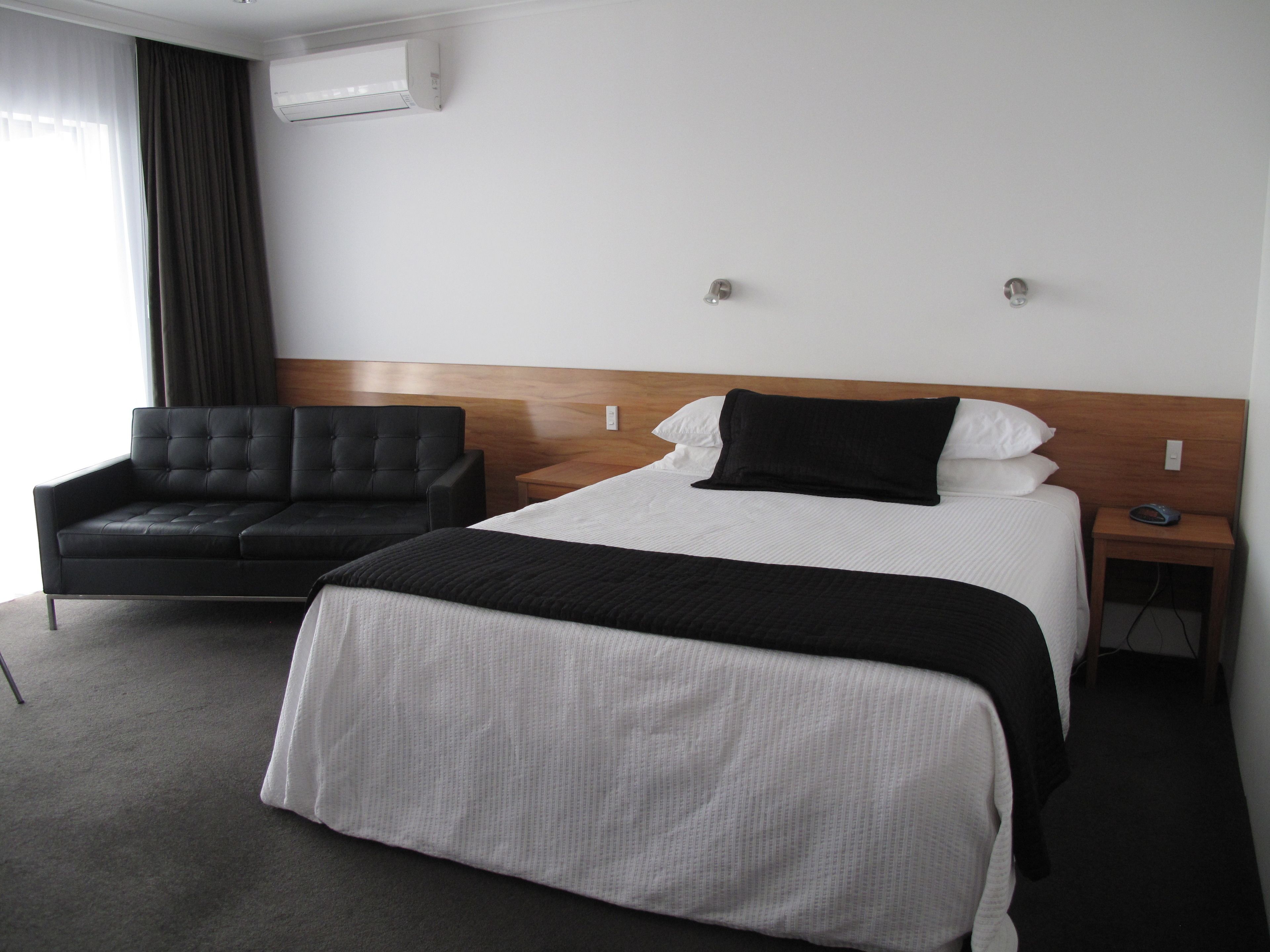 Une chambre d’hôtel avec un lit, un canapé noir, une tête de lit en bois et une table de chevet avec un téléphone.