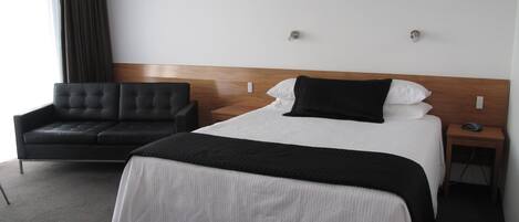 Une chambre d’hôtel avec un lit, un canapé noir, une tête de lit en bois et une table de chevet avec un téléphone.