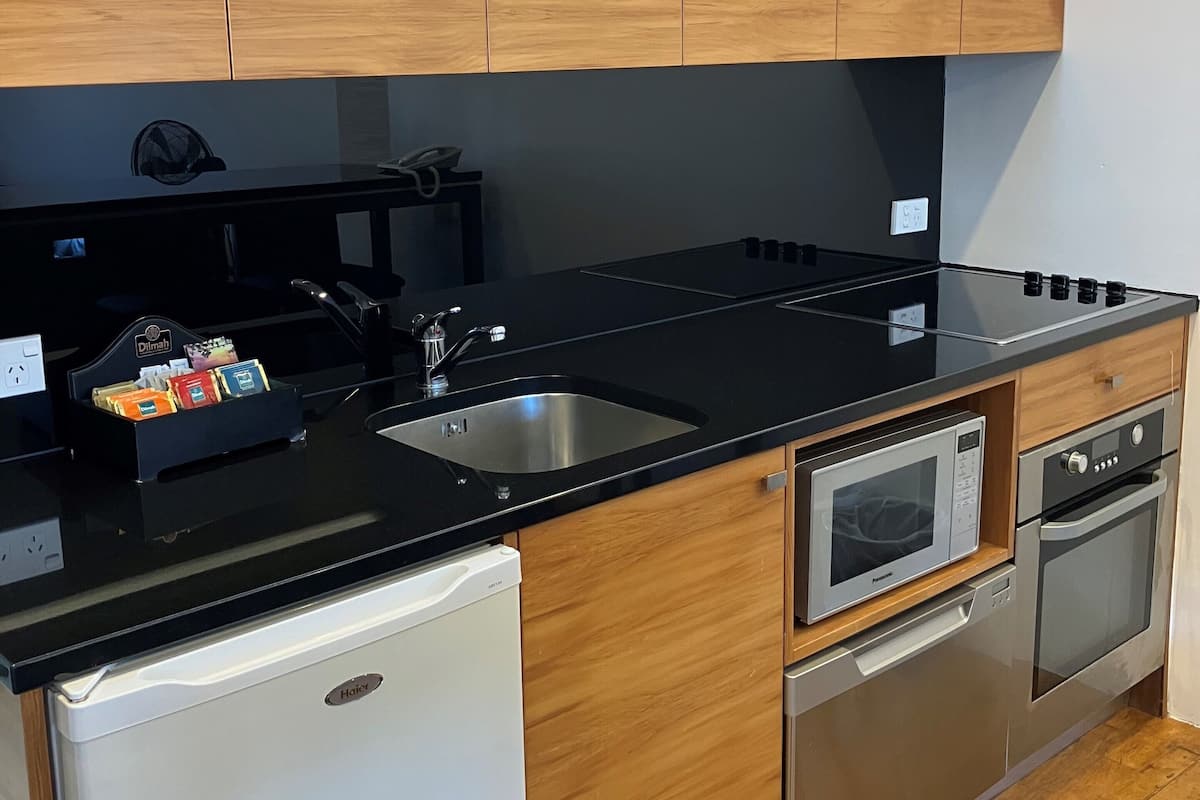A modern kitchen with wooden cabinets, a black countertop, a stainless steel sink, a microwave, and a dishwasher.