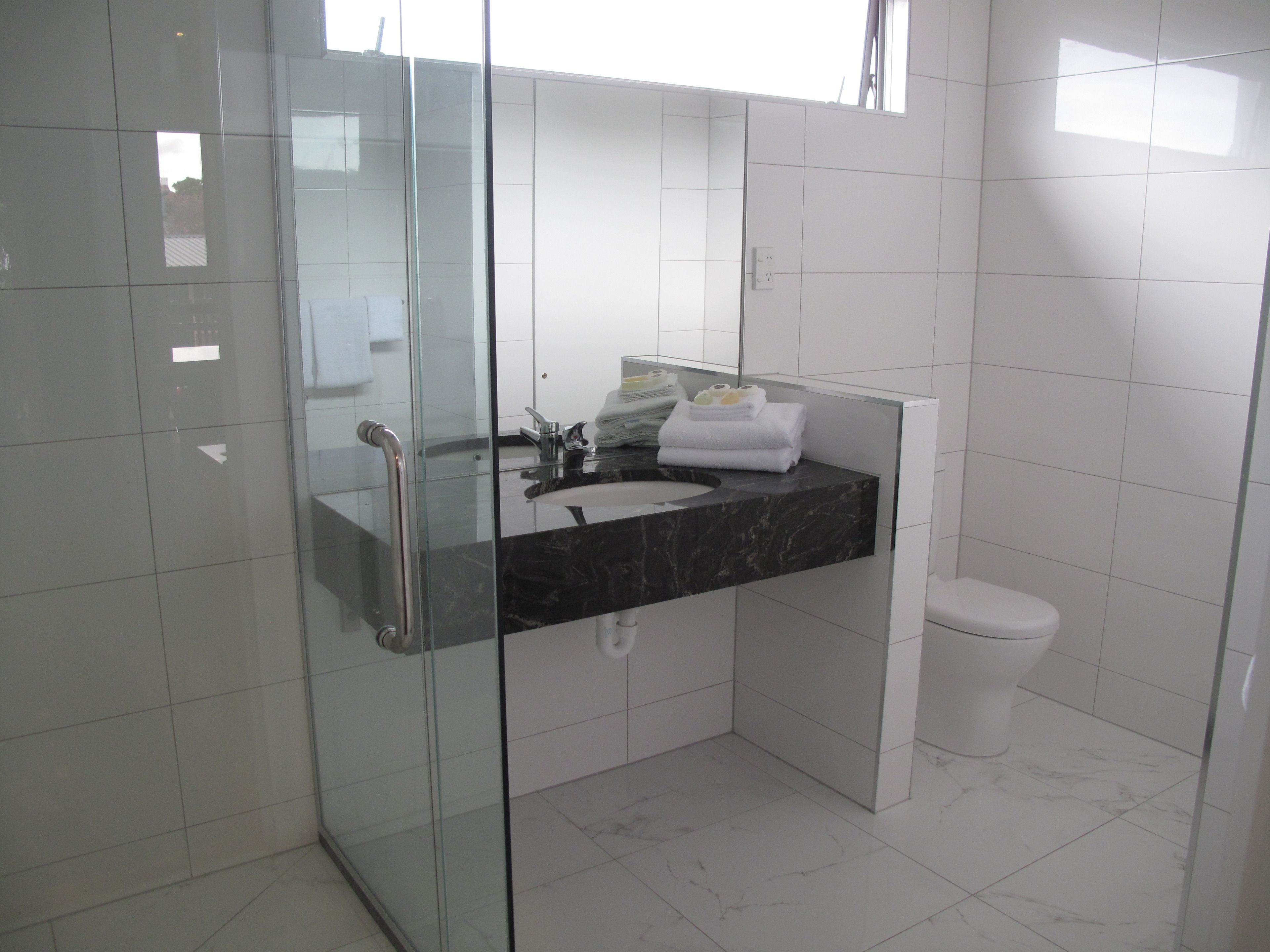A modern bathroom with a glass shower enclosure, a marble sink, and a white toilet.