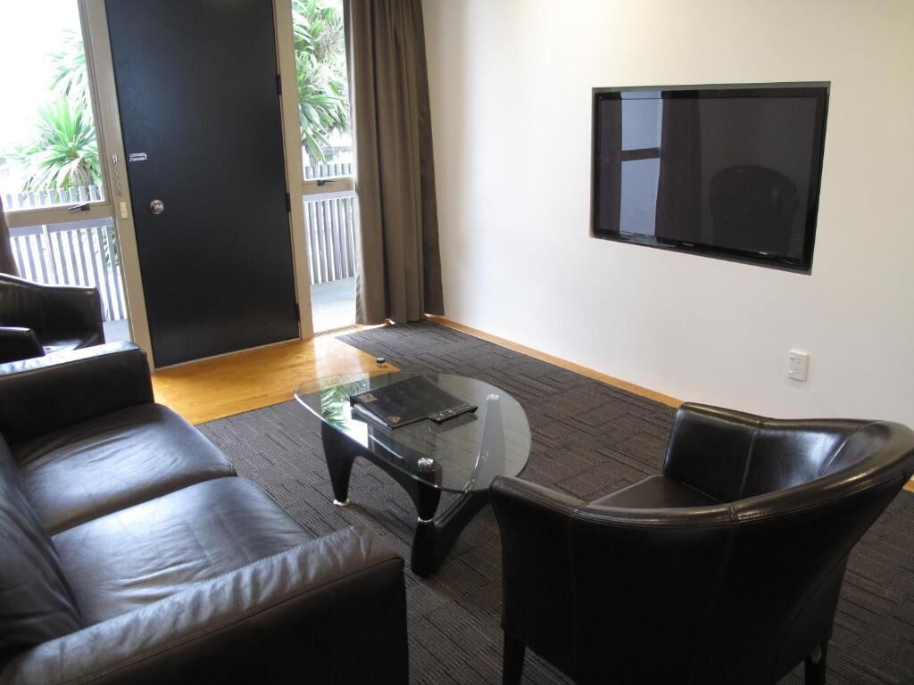 A modern living room with a leather sofa, a glass coffee table, and a flat-screen TV mounted on the wall.