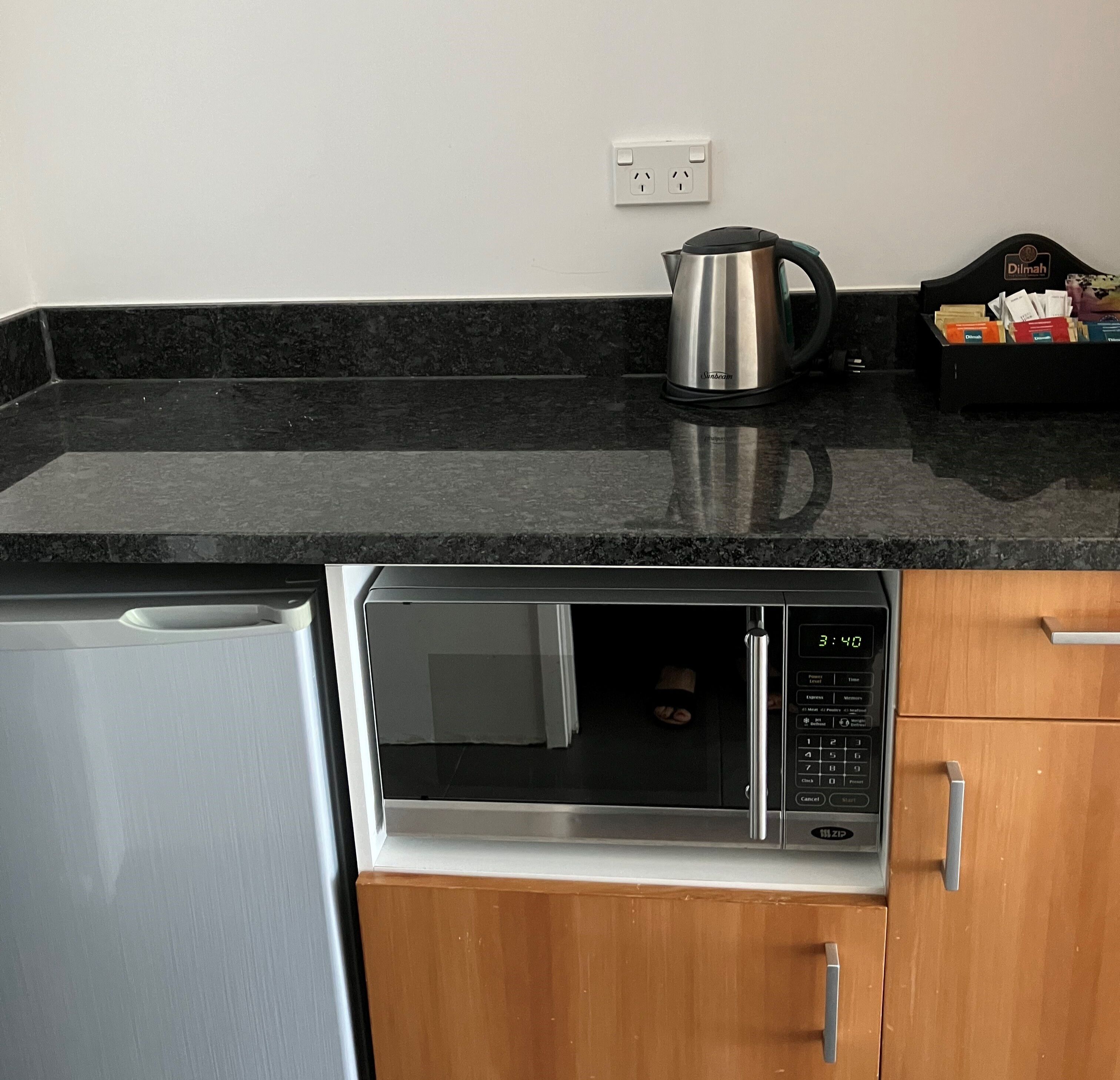 Una cocina con un refrigerador de acero inoxidable, un horno microondas y una tetera sobre la encimera.