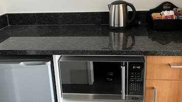 A kitchen with a stainless steel refrigerator, a microwave oven, and a kettle on the countertop.