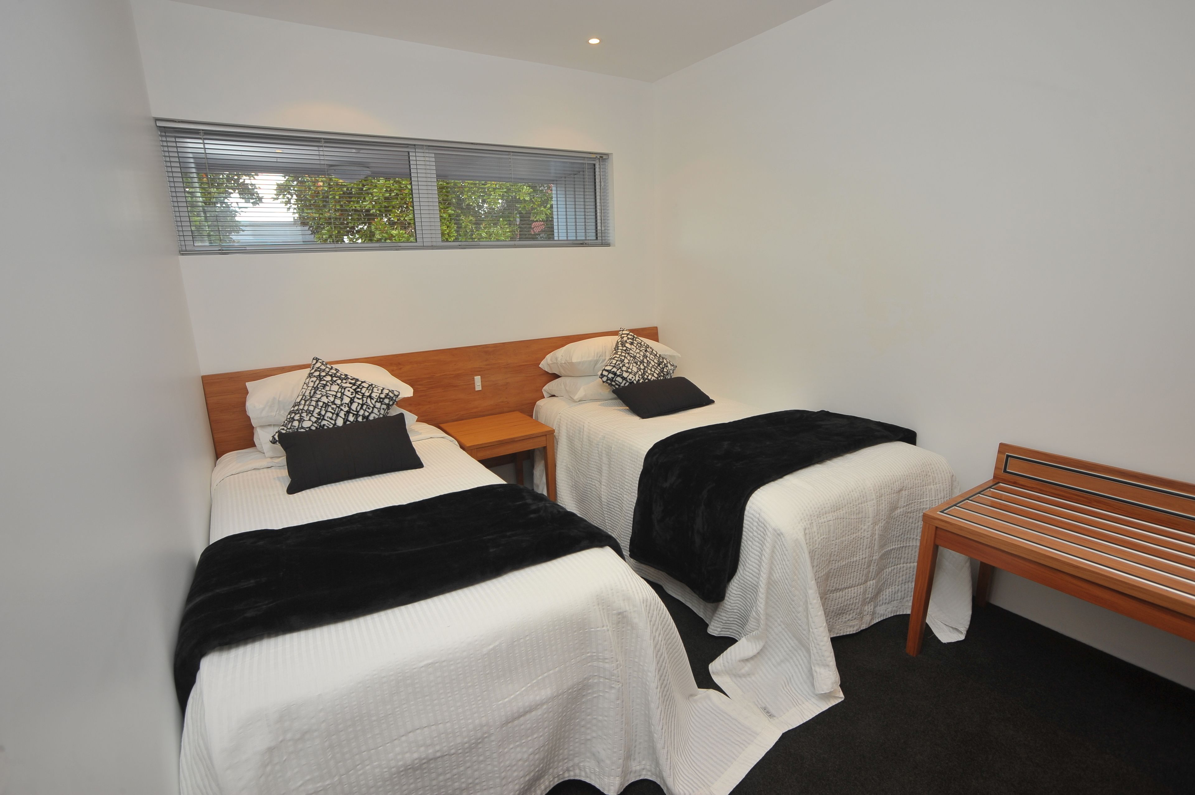 A bedroom with two single beds, a wooden bench, and a window with blinds.
