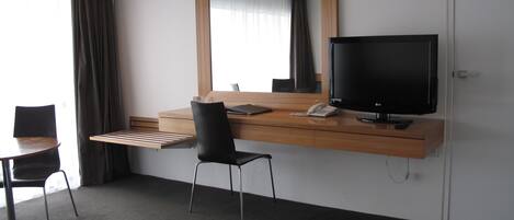 Una habitación de hotel con un escritorio de madera, una silla negra, un televisor y un teléfono.