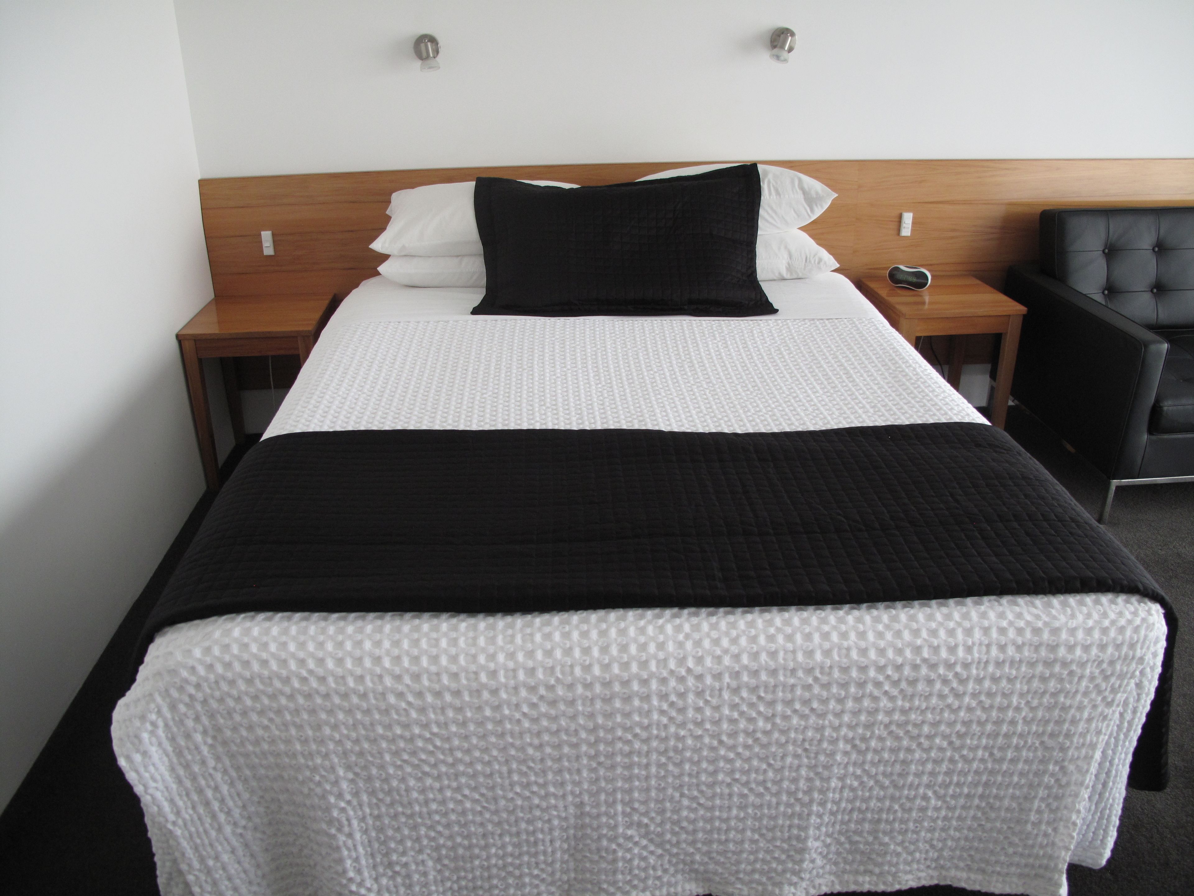 A neatly made bed with white and black bedding, a wooden headboard, and a black chair to the side.