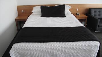 Una cama bien hecha con ropa de cama blanca y negra, un cabecero de madera y una silla negra al lado.