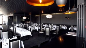 Un ristorante con diversi tavoli apparecchiati, illuminato da lampade a sospensione e caratterizzato da un design moderno.