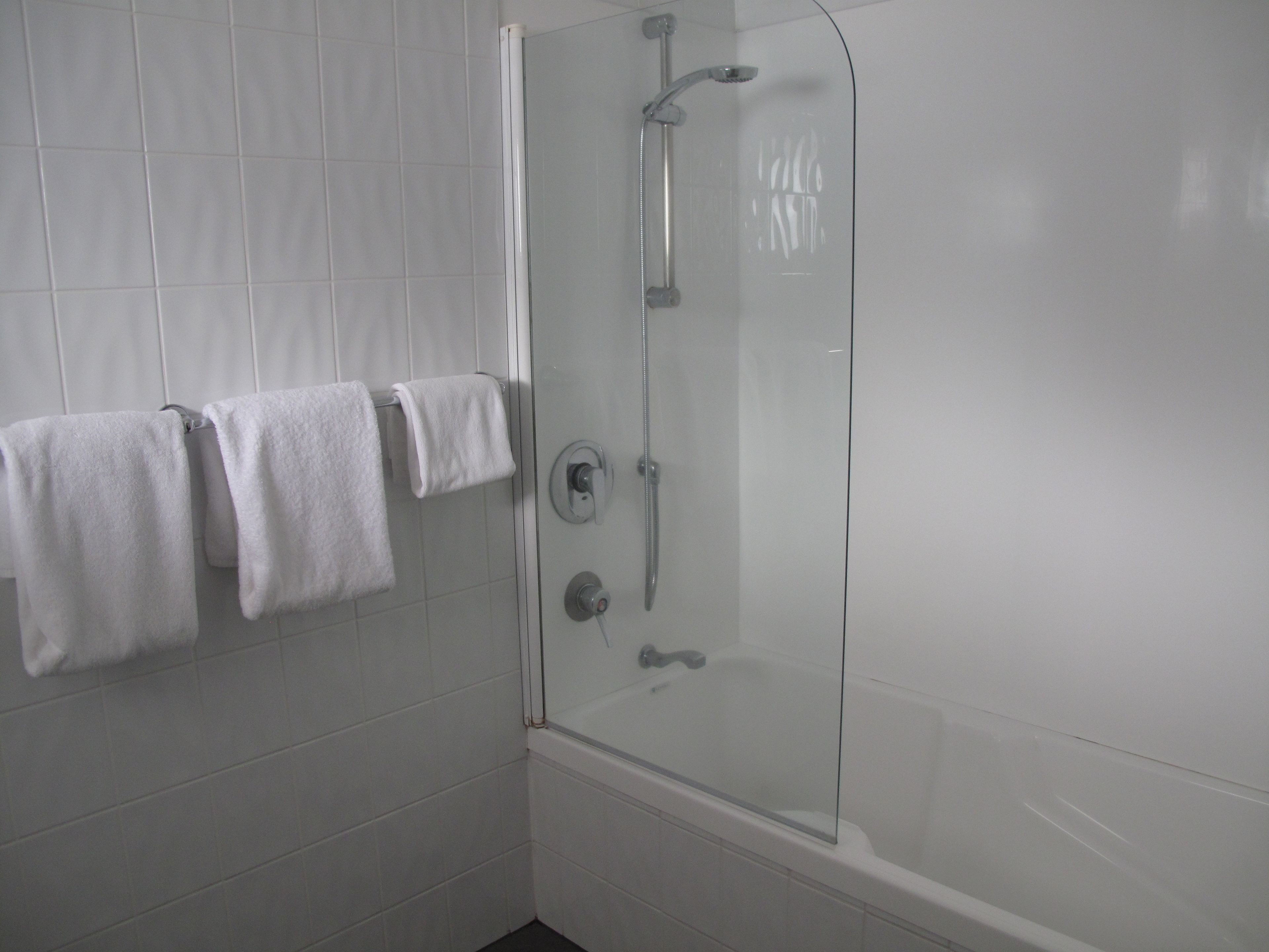 A modern bathroom with a glass-enclosed shower, white tiles, and three neatly hung towels.