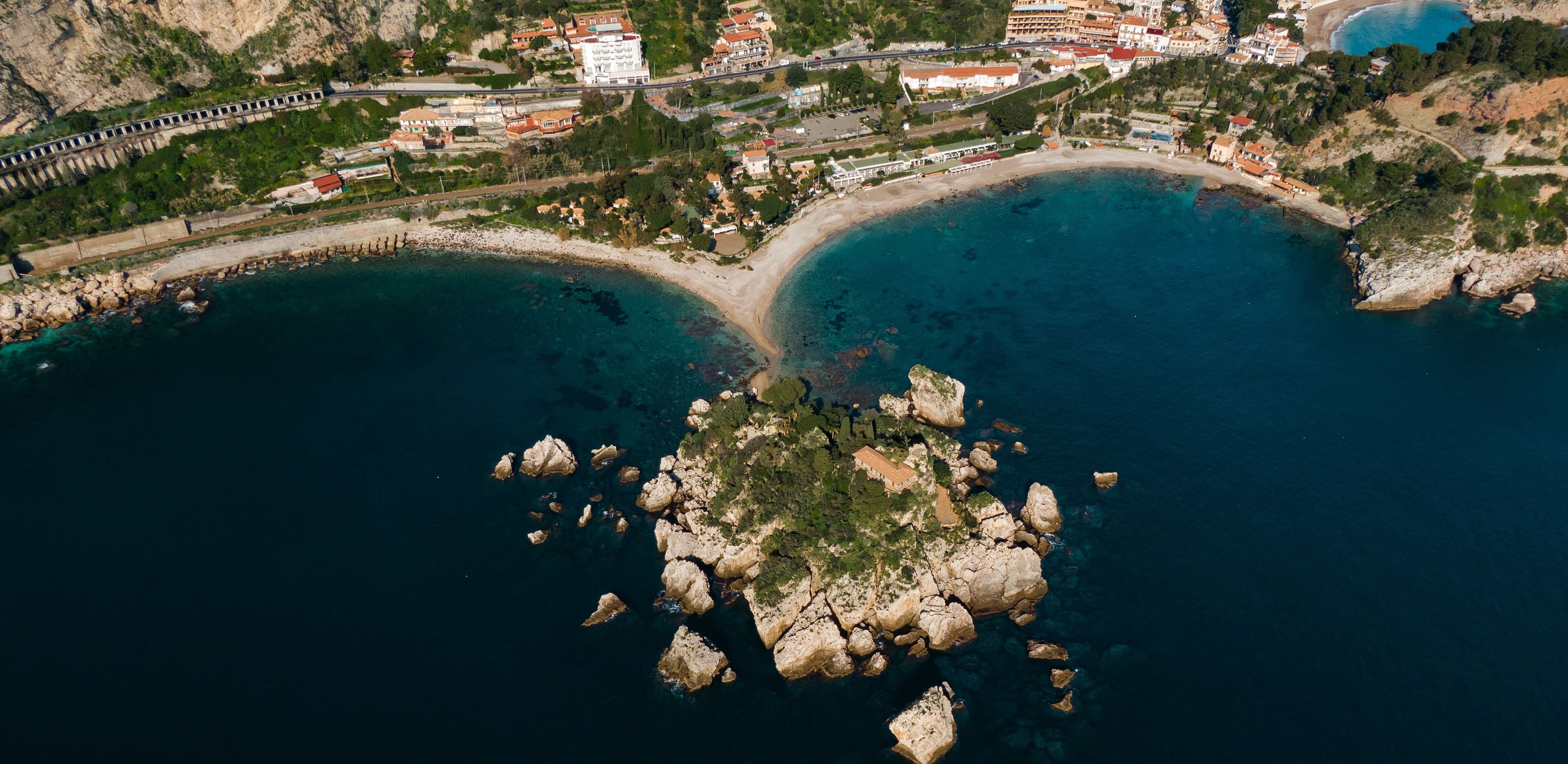 Vista aérea de una zona costera con afloramientos rocosos, una playa y edificios.