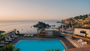 Una piscina en la azotea con sillones de descanso y vistas al mar y a la costa rocosa.