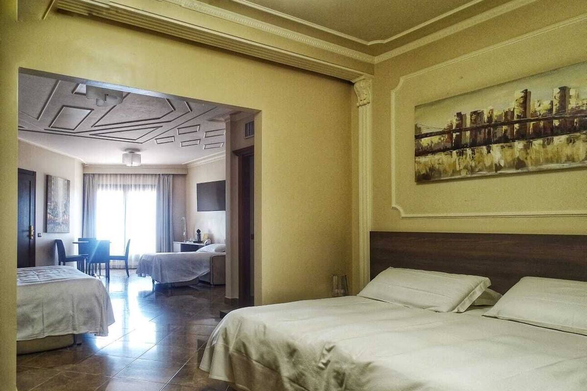 A hotel room with two beds, a dining area, and a cityscape painting.