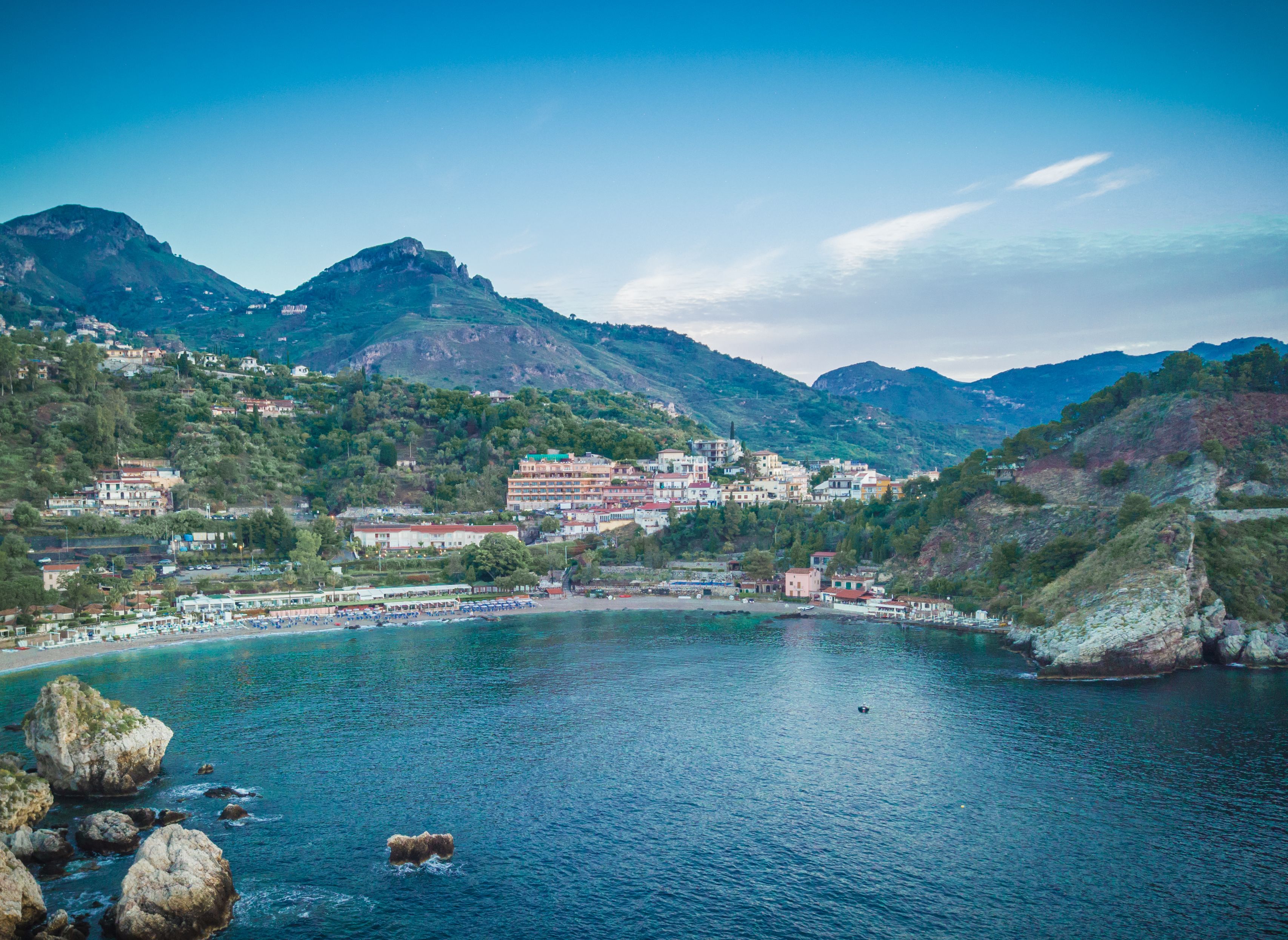 A coastal town with buildings along the shoreline, a large body of water, and mountains in the background.
